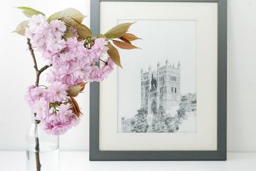 schwarz-weiss-Bild der Notre Dame in einem schwarzen Rahmen auf einem weissen Tisch mit einer Blüte im Vordergrund