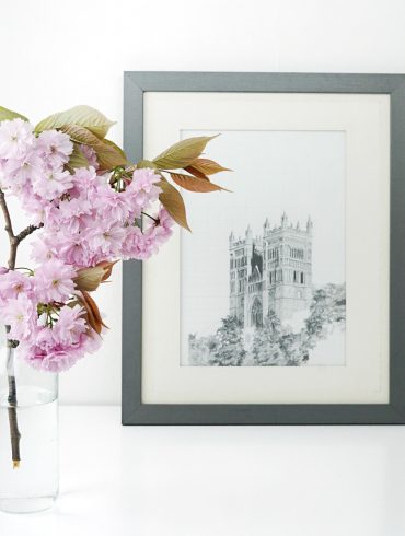 schwarz-weiss-Bild der Notre Dame in einem schwarzen Rahmen auf einem weissen Tisch mit einer Blüte im Vordergrund