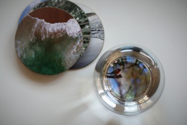 Blick von oben auf Untersetzer mit Fotos und Wasserglas